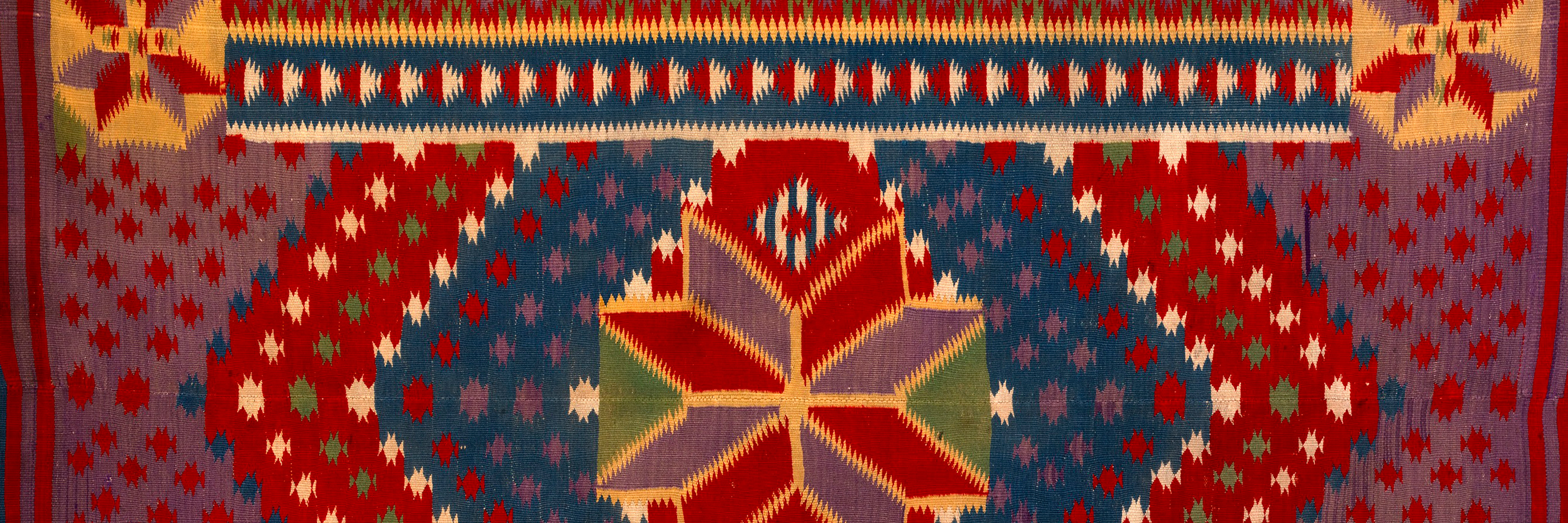 A close up detail of a colorful patterned tapestry.